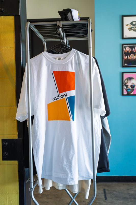 White t-shirt with orange and blue design hanging on a rack against a blue wall.