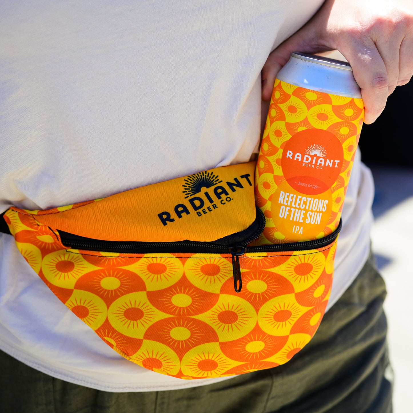 Person holding a can of Radiant Beer Co. Reflections of the Sun IPA with a matching fanny pack.