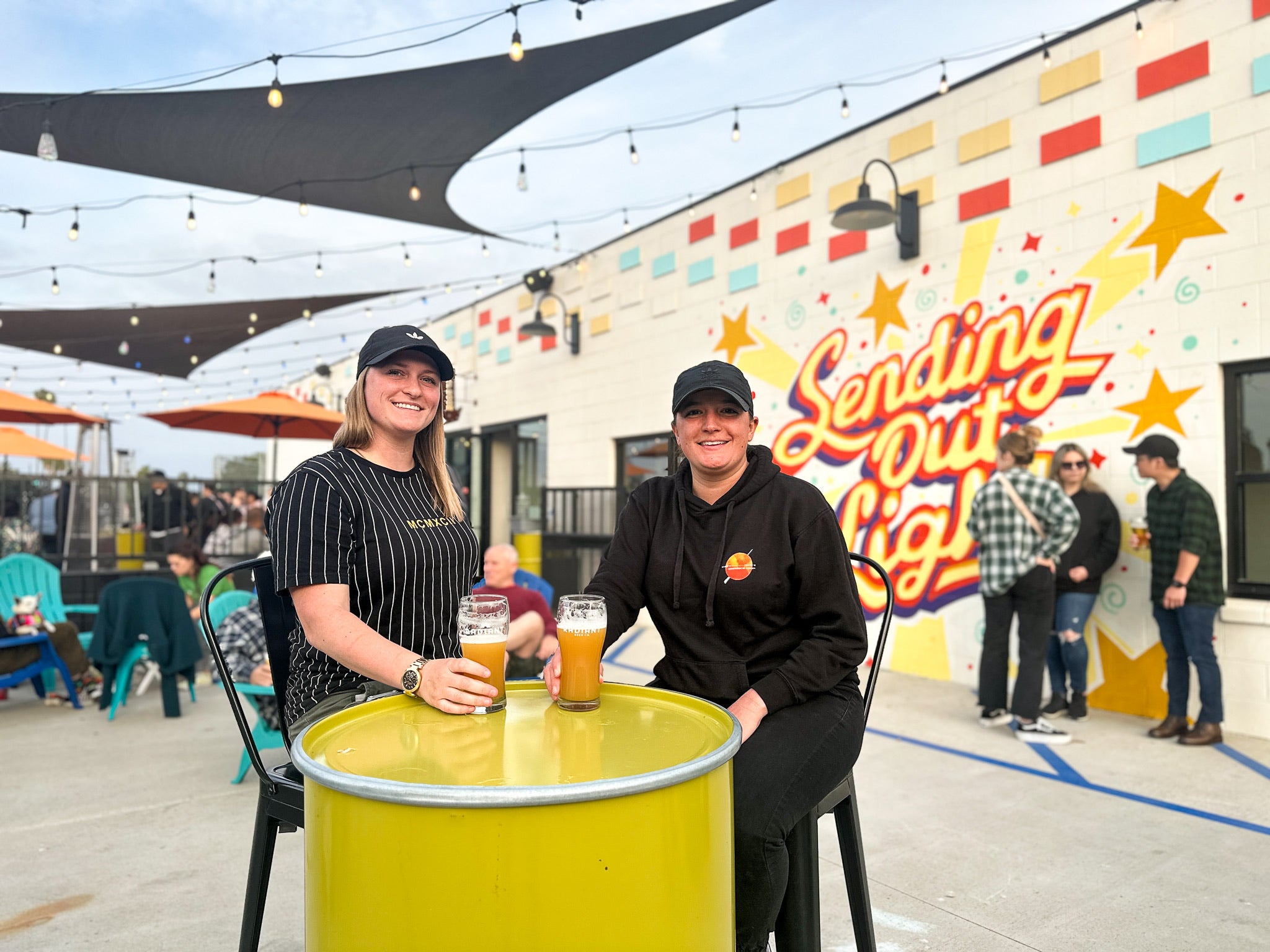 2 individuals sit with hazy ipas in front of the Radiant Sending Out Light Mural