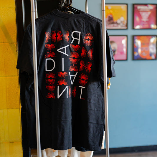 Black t-shirt with red and white graphic design on a hanger against a colorful wall.