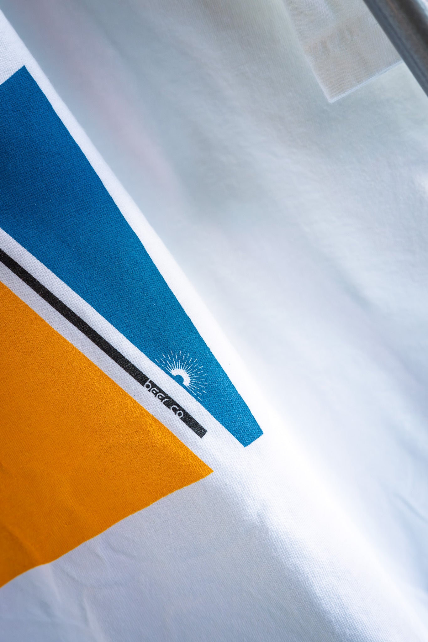 Close-up of a white shirt with blue and orange design and a visible brand logo.