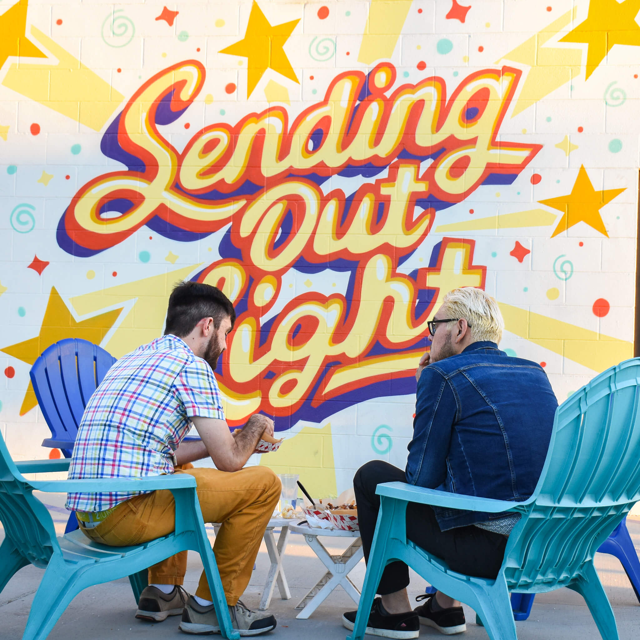2 customers set in chairs in front of the sending out light mural 