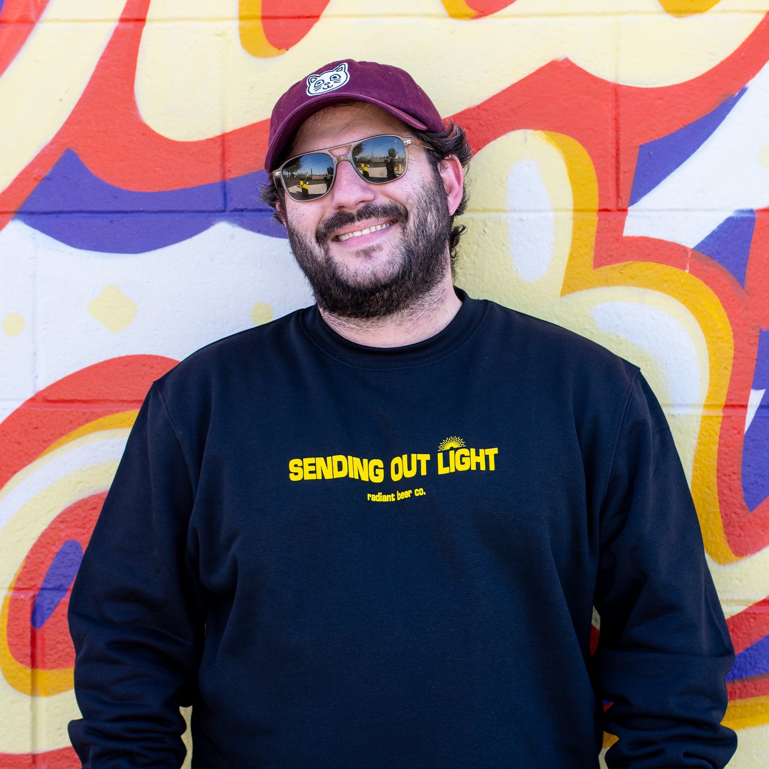Man wearing a black sweatshirt with 'SENDING OUT LIGHT' text in front of a colorful mural.