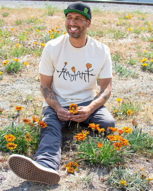 Team Member in a field of flowers with a cream shirt that says radiant with flowers 